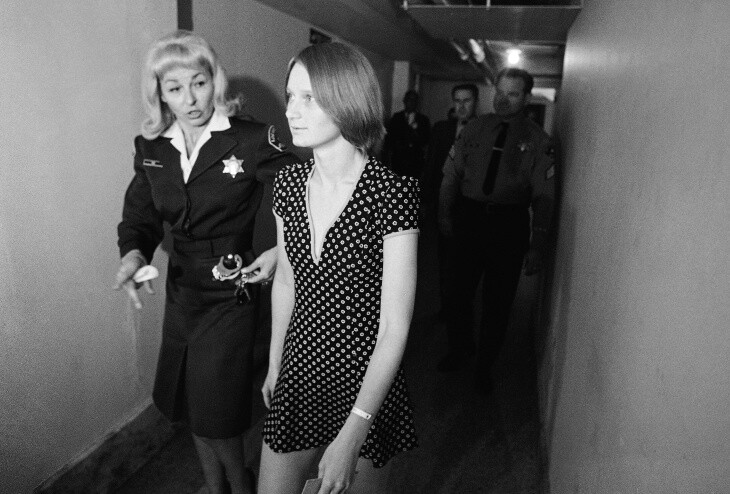 Brunner wears a polka dotted minim accompanied by an officer in a skirt suit and wearing a star badge.