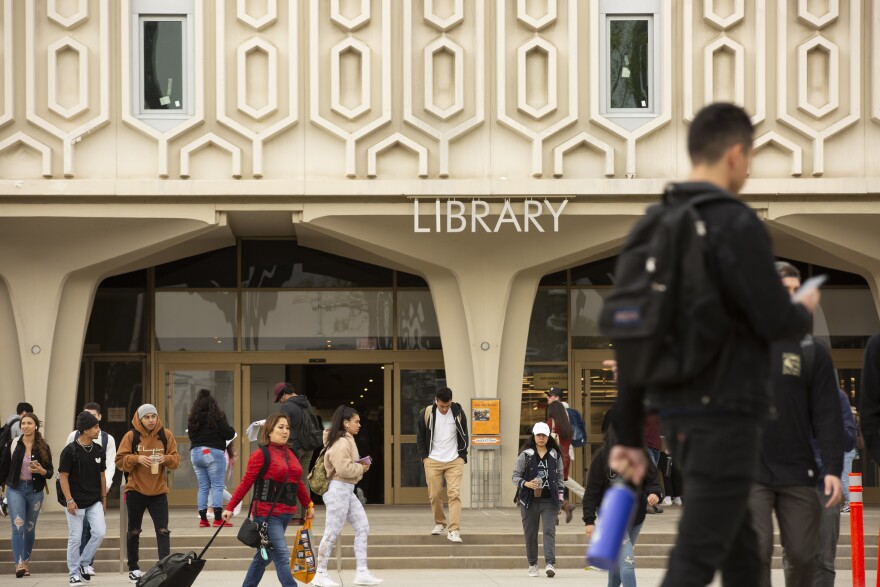 People walk in front of a large white building that says "Library."