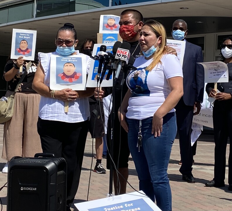 At a July 9, 2021 rally protesting the killing of Nicholas Burgos, his mother Maria Guzman, on the left holding a poster with a drawing of Burgos under the words "Justiice for Nick Burgos," his brother Benjamin Burgos, in the middle, and his sister María Burgos, on the right, stand in front of microphones addressing the rally.