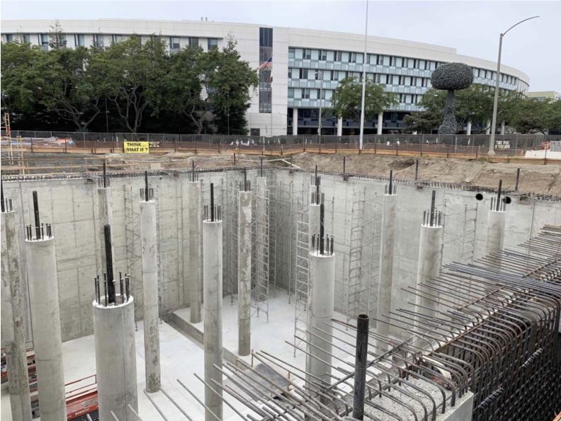 A huge open concrete pit with pillars below a circular building.
