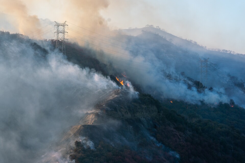 Fire burns the side of a mountain with smoke coming out of it.