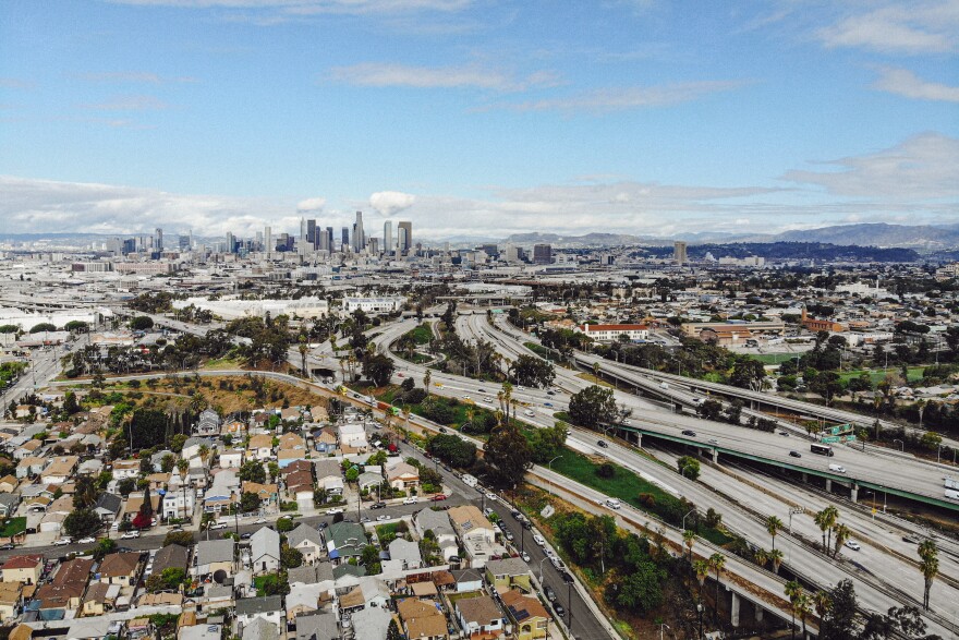 An aerial shot of multiple Los Angeles area freeways criss crossing one another. The Downtown Los Angeles skyline can be seen in the background.
