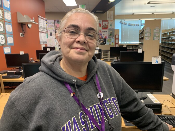 A woman with gray hair, pulled back, wearing a gray sweatshirt with the word "Washington" in purple and a purple lanyard, poses for a photo.