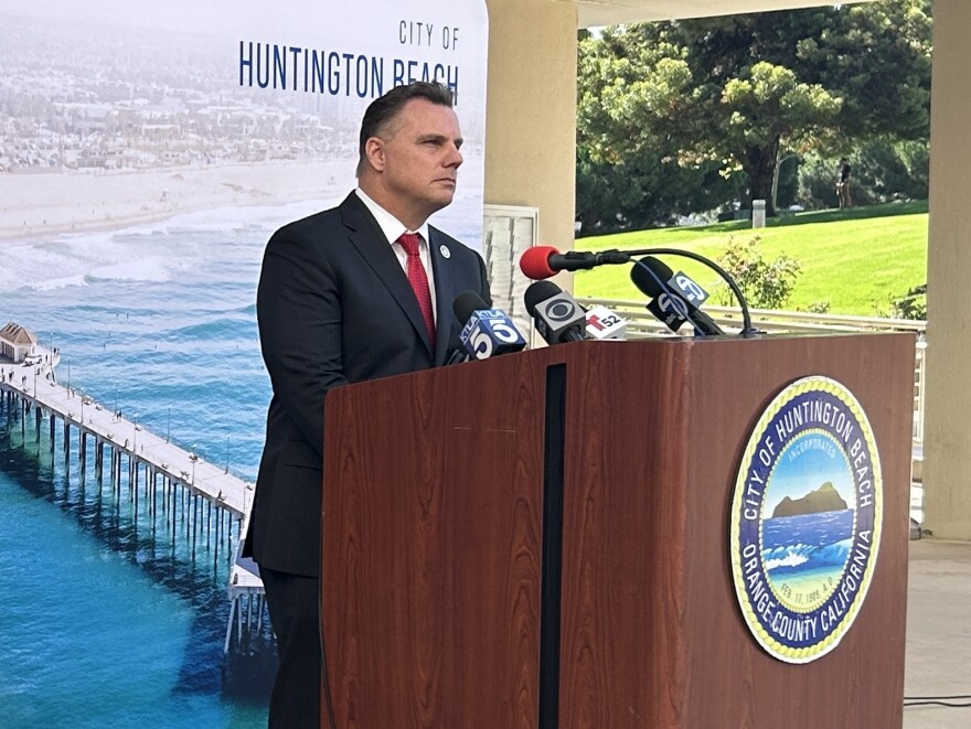 A man at a podium with the seal of the City of Huntington Beach on it and a large image of the pier and the beach behind him.