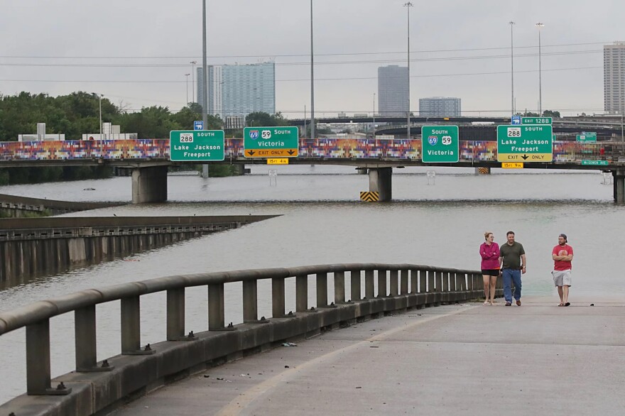 Three people walk alongside a freeway that's been flooded by water.