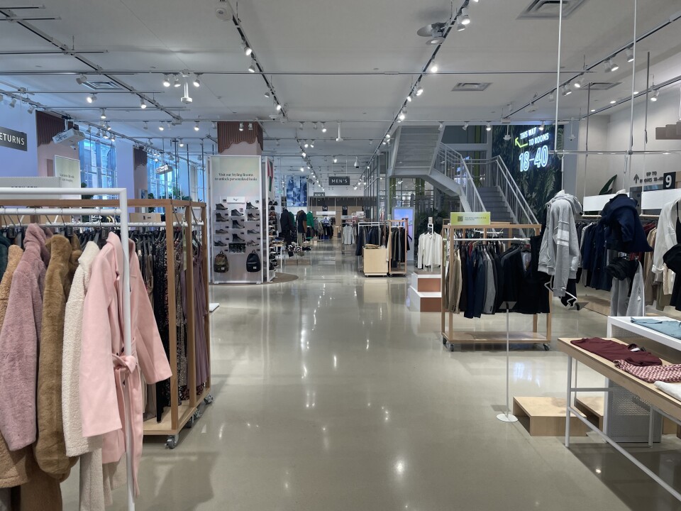 The inside of a retail store, with clothing racks, shoe displays, and tables with t-shirts in view. The store is empty.