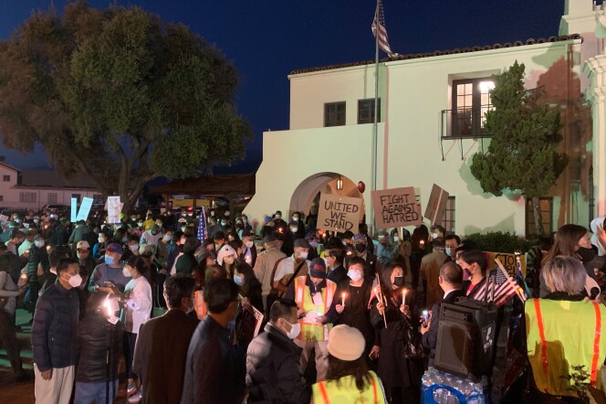 A crowd of hundreds amasses in front of an old Spanish mission for a vigil. People are holding candles and you can see signs that read "United We Stand" and "Fight Against Hatred."