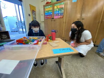 A transitional kindergartener at Harding Elementary in Sylmar plays with blocks as Kelly Gonez, president of the L.A. Unified school board, looks on. The student has been given her own set of toys; shared toys, materials and supplies are not allowed in L.A. Unified School District classrooms under reopening guidelines for hybrid instruction.
