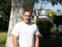 A man stands in front of a tree in a residential neighborhood.