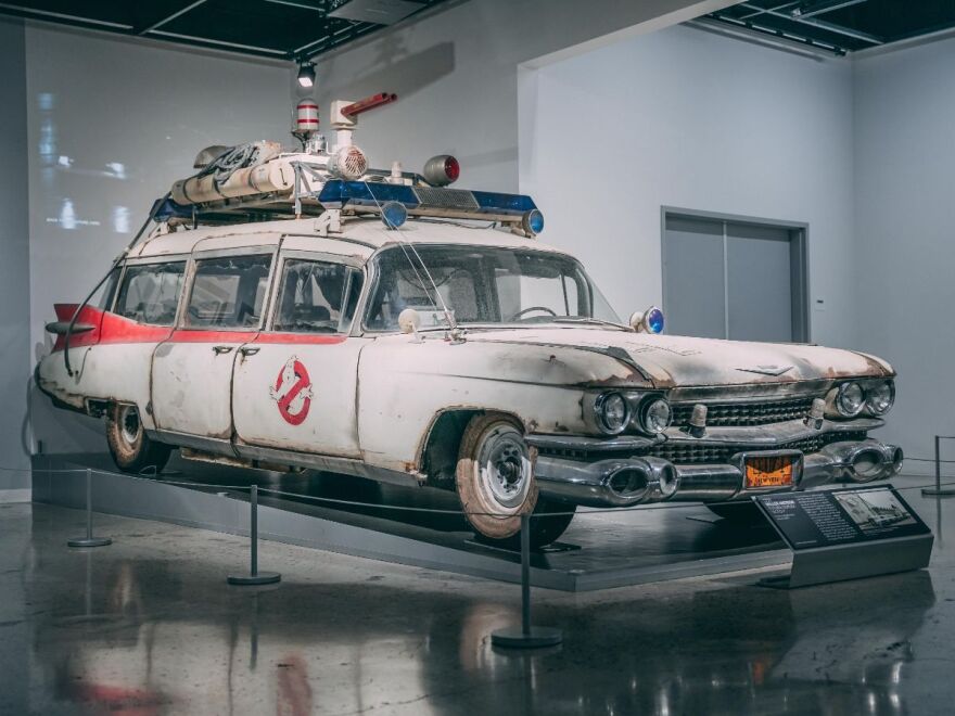 A white beat up station wagon with the ghost busters logo on the side and equipment on the roof