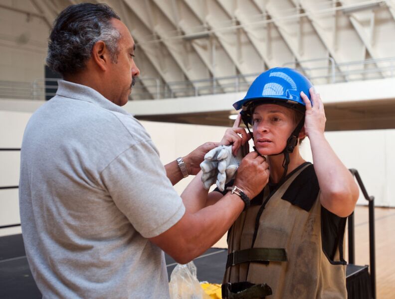 Al Perez of the LAFD Legal Liaison Unit helps applicant JJ Edgmon put on a helmet before her first practice try of the Candidate Physical Ability Test. 