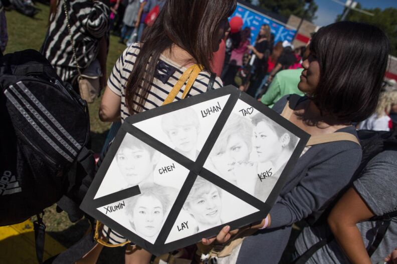 A K-Pop fan holds a handmade sign with members of the Korean pop supergroup Exo on it. She used the sign as a sunshade in the 90-degree heat on Sunday.