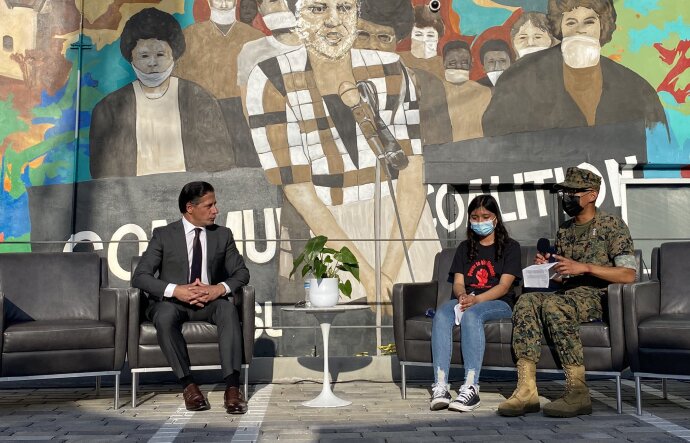 Under a mural featuring Karen Bass, the LA Unified superintendent talks with two masked students.