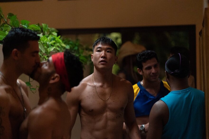 A shirtless Joel Kim Booster at a party with men, some kissing.