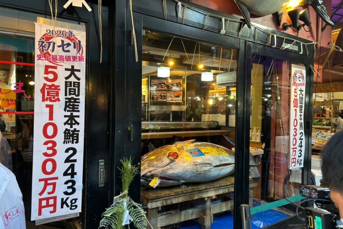 The storefront of a Japanese fish market or restaurant, prominently featuring a massive tuna displayed inside on a wooden platform.  
