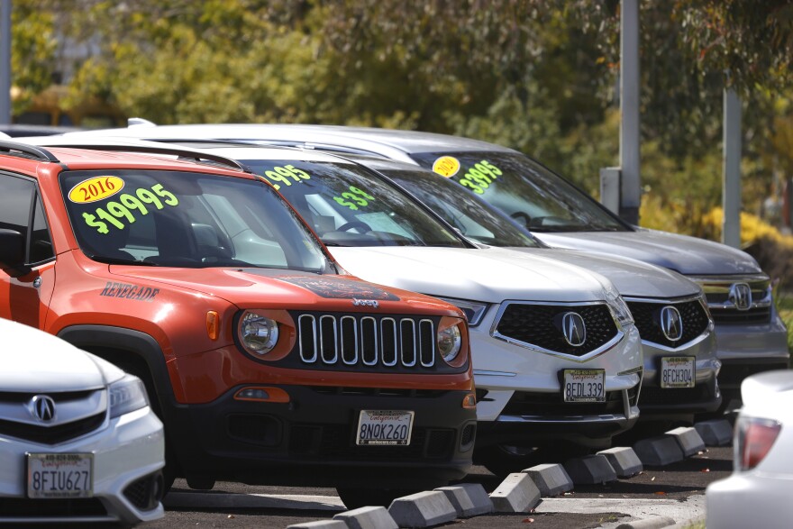 Used cars parked in a row have sticker prices on their windshields including a 2016 red Jeep for $19,995.