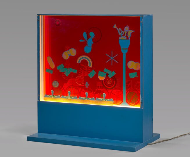 A standing, blue box holding illuminated red, yellow, green and blue artwork. It's displayed in a gray room. 