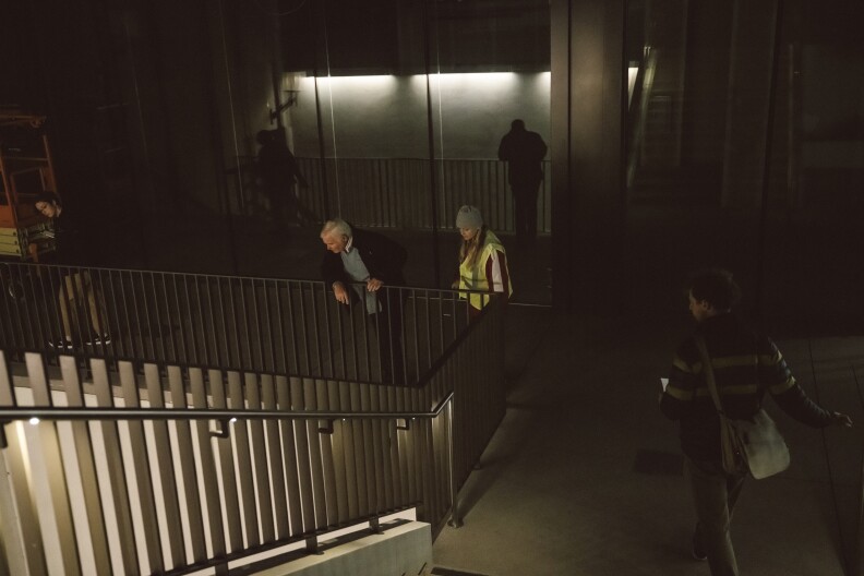 Four people stand near a railing at night looking down.