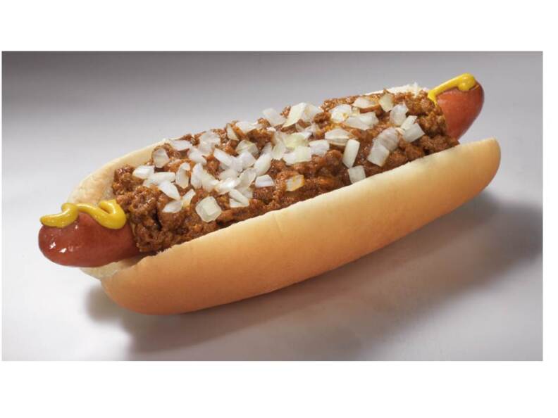 A hot dog in a split bun sits with chili, onions and mustard on top