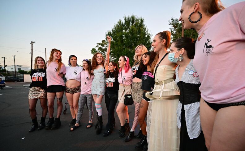 Women lock arms in a wor in a parking lot, some wearing T-shirts that read "Strippers United."