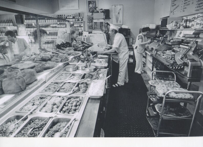 A man and a woman working behind the counter at a deli.