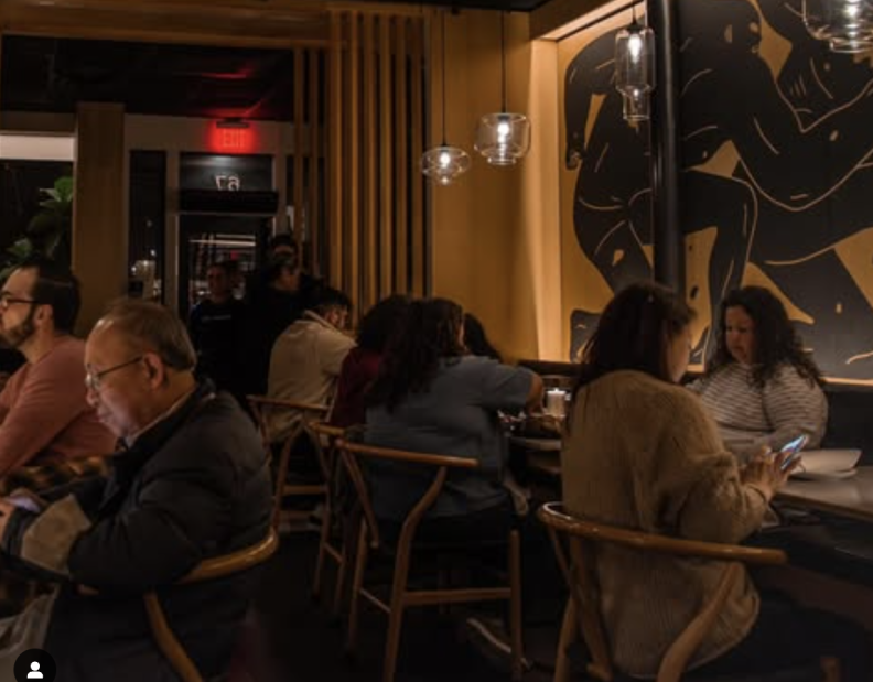The interior of a restaurant at night time; it's a cosy space with dim lighting, and full tables.