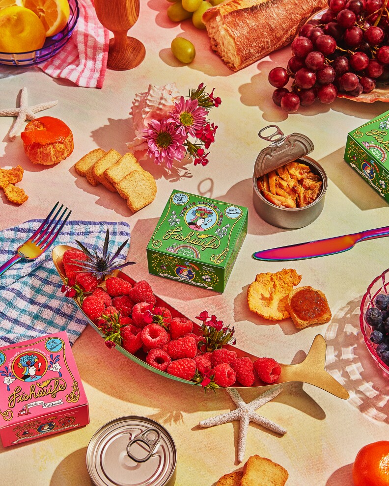 An assortment of raspberries, tinned fish, grapes, olives, half a baguette and bread with jam.