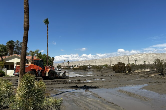 A wide shot of muddy roads in a residential neighborhood. An orange dozer to the left works to clear the road. 