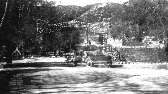 A car speeds away from the lodge onto New York Avenue. The stone archway that still stands can be seen in the background. 
