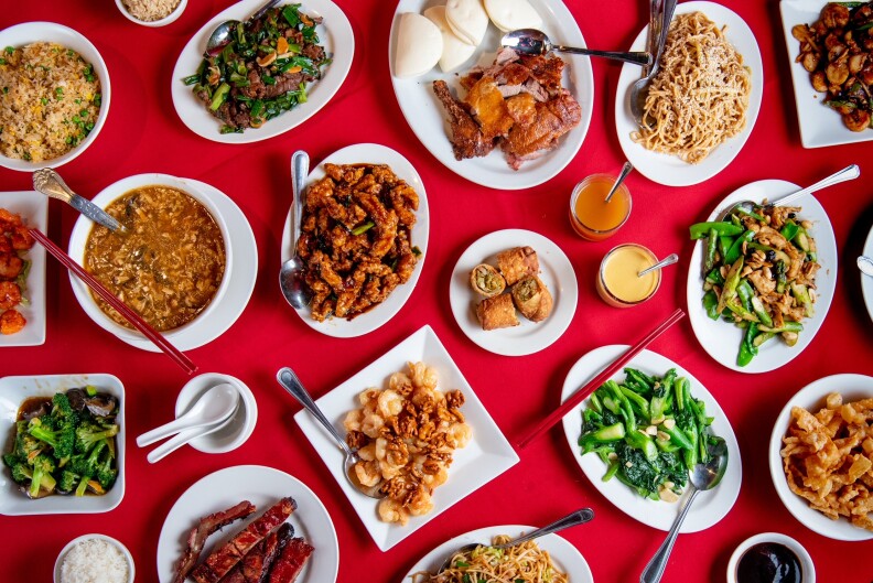 an overhead shot looking down at dozens of dishes of chinese food on white plates on a red tablecloth