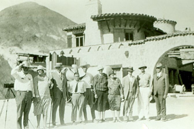 A group of people standing in front of a mansion in the desert.