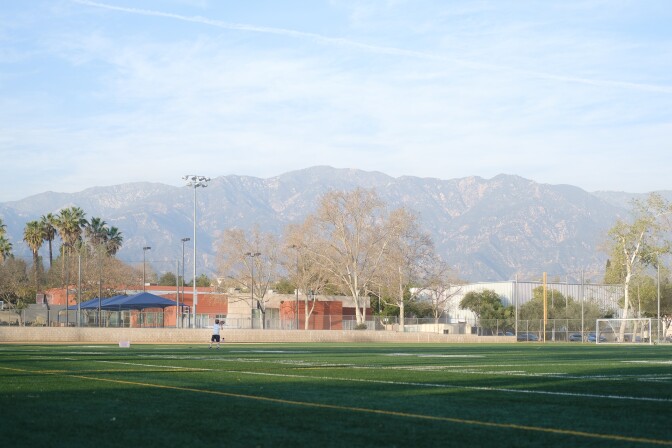 An empty football field with several parks facilities buildings in the background.