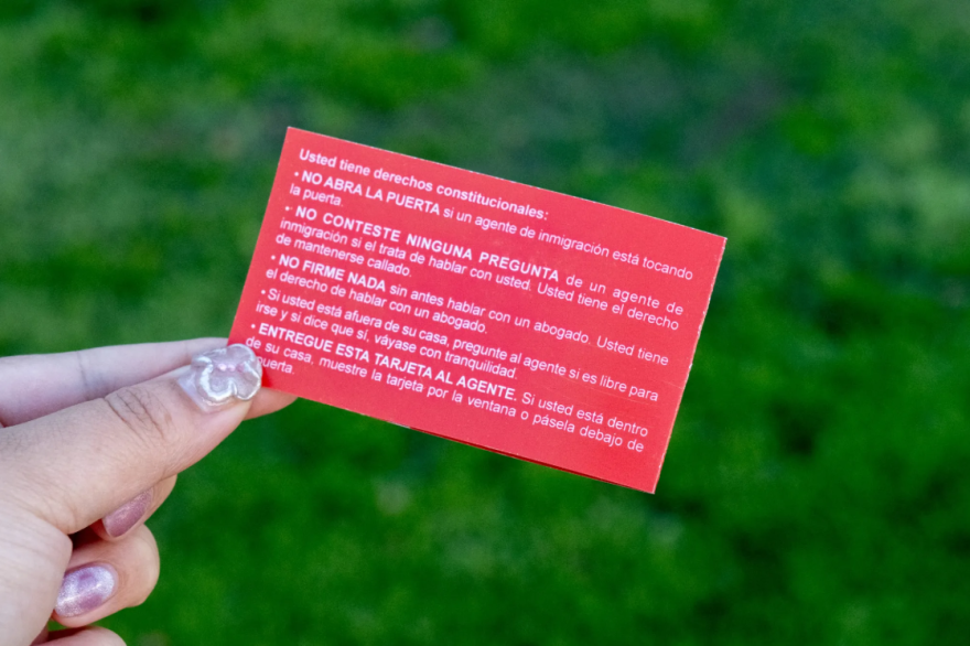A hand holding the corner of a red card the size of a business card. It has text in Spanish.
