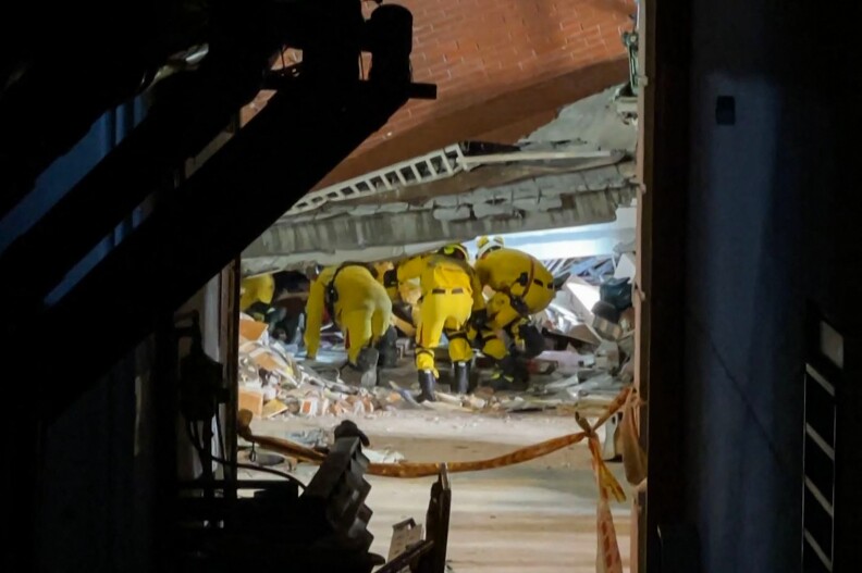 Rescue workers search under a damaged building.
