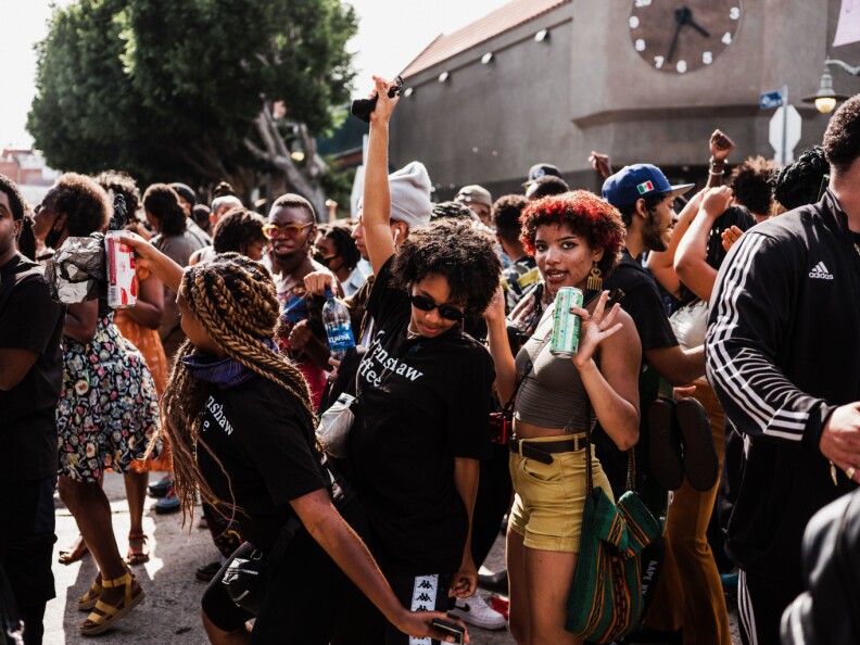 People, all or most of them Black, dance outside in front of a building with a clock on the front.