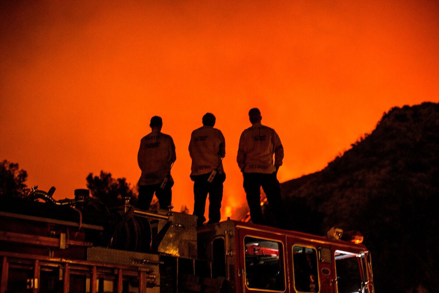 Firefighters standing on their fire truck watch as the Bobcat Fire burns on hillsides behind homes in Monrovia.