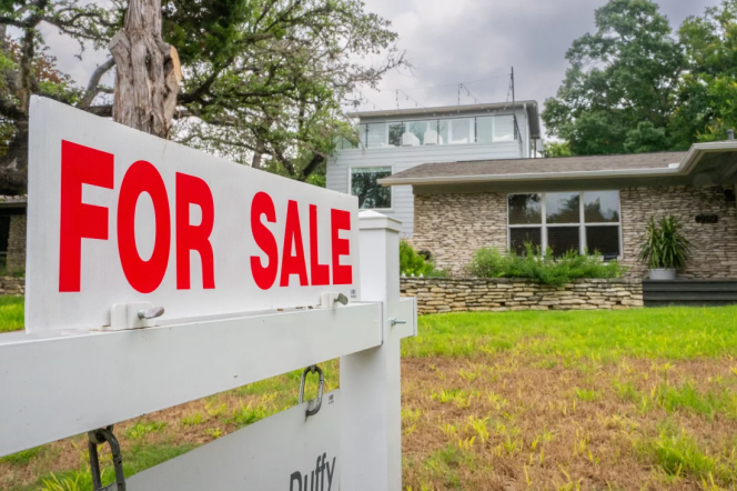 sign in foreground of photo in front of a house and overcast sky reads "FOR SALE" in all caps + red letters.