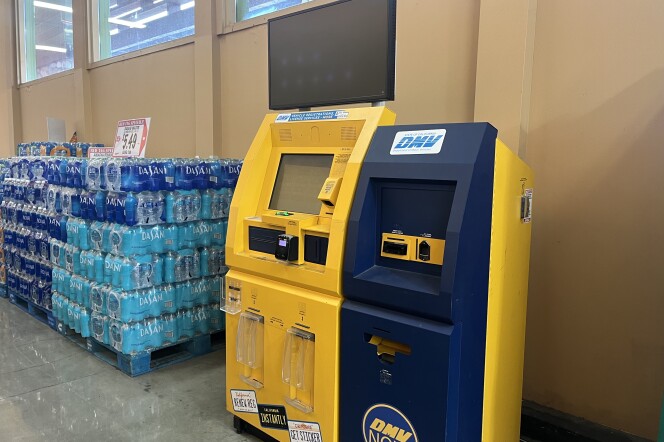 A blue and yellow self-service kiosk covered in DMV logos stands inside a grocery store.