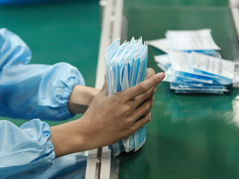 A person's hands gold a stack of blue surgical masks.