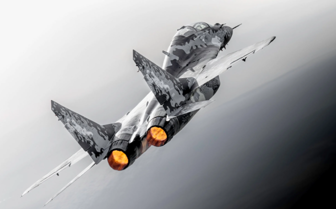 A camouflage-patterned fighter jet climbs steeply with afterburners glowing orange from its twin engines.