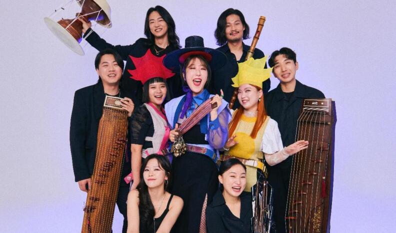 Nine Korean musicians hold traditional Korean instruments while smiling for the camera