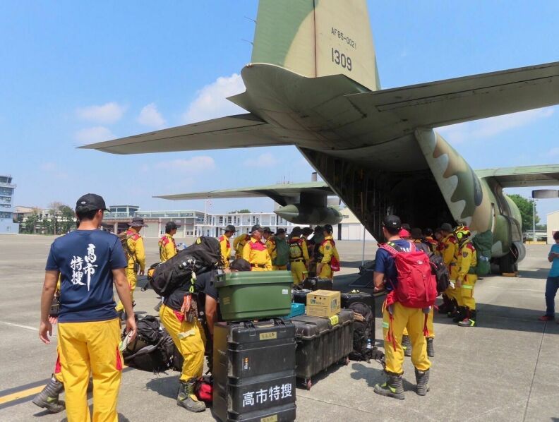 A line of aid workers file in and load supplies into the back of a large green plane.