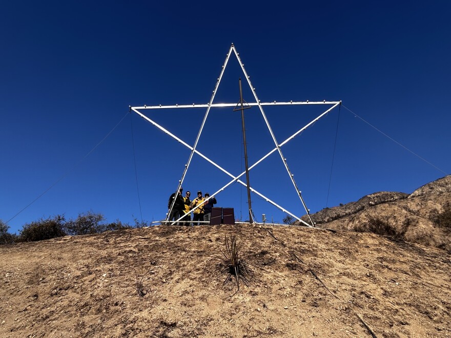 A group of 4 people behind a gigantic star structure on top of a hillside.