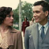 Florence Pugh and Cillian Murphy walk down a street together. Their clothes and surroundings indicate that they are in the 1950s. Pugh wears a tan collared coat with a champagne blouse underneath. She looks over a Murphy with sternly, seemingly annoyed at him. Murphy smiles back at her through closed lips, seemingly amused at Pugh's disdain. He wears a grey three piece suit and tie. 