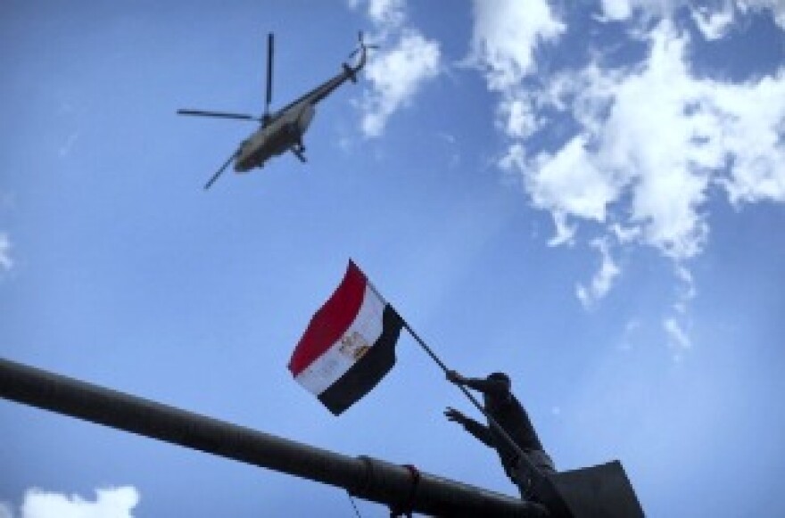 A helicopter hovers overhead as an Egytpian demonstrator wave his flag from atop of a traffic light post in central Tahrir Square in Cairo on January 31, 2011, on the seventh day of mass protests calling for the removal of Egypt's President Hosni Mubarak.