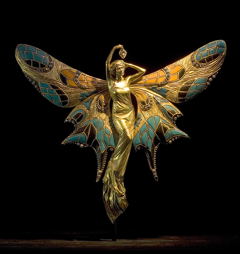A woman painted in all gold is seemingly suspended in the air with elaborate butterfly wings attached to her back.