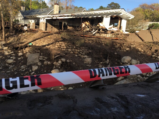 Warning tape blocks a damaged bridge on East Valley Road over Montecito Creek, while behind the creek, a brown mud line on the white house shows how high the debris flowed during the Jan. 8, 2018 rainstorm and flood.