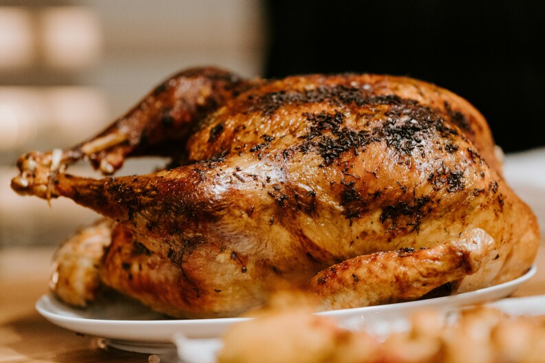 A roasted golden brown turkey sits on a white plate against a blurry background.