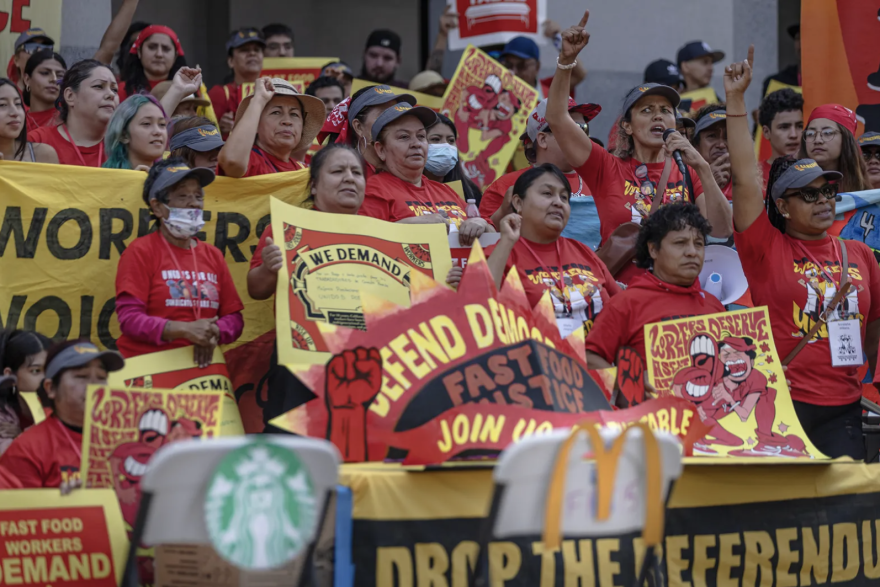 A large group of fast-food workers, many wearing red shirts and carrying red and yellow signs. They appear to be in front of a building.