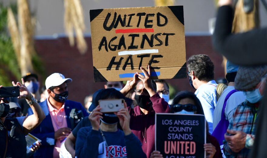 A dozen of people, some wearing masks and holding signs that read "United Against Hate," march outside.